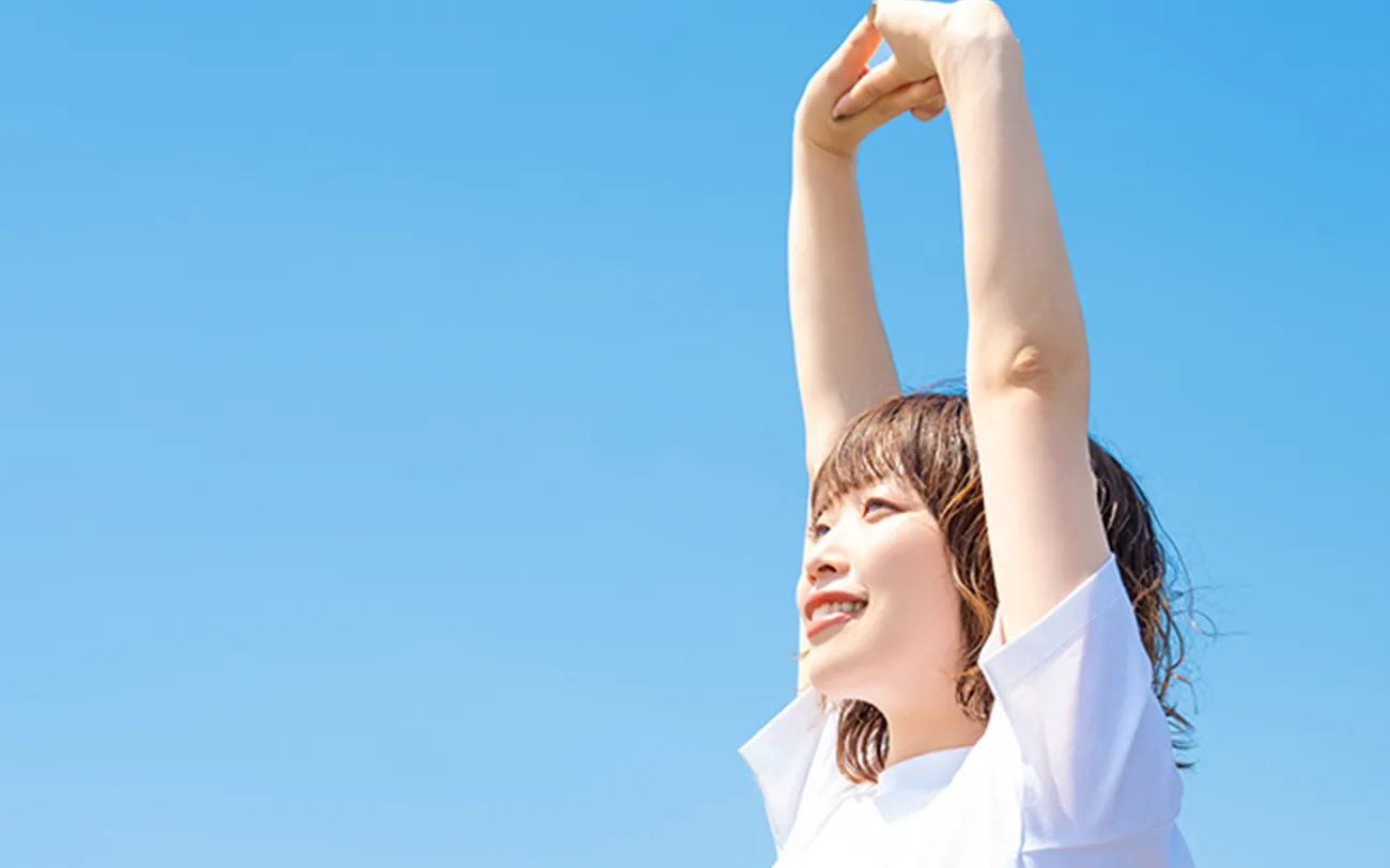 笑顔の女の人が空に向かって伸びをしている。